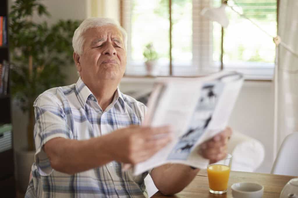 a male senior having a hard time reading a news paper